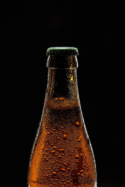 Close-up de garrafa de cerveja castanha com tampa verde contra bolhas de fundo preto de cerveja espumosa de lager