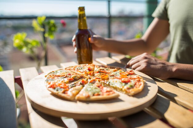 Close-up de garrafa de pizza e cerveja na mesa. Mão masculina segurando a garrafa sobre a mesa com fatias de pizza. Comida, menu, conceito de café