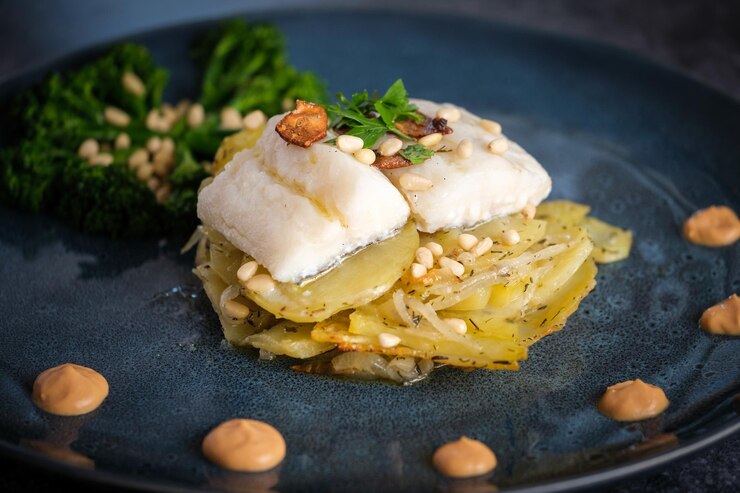Foto close-up de gratinho apetitoso com filé de peixe branco coberto com verduras e nozes de pinheiro perto de brócolis em prato de cerâmica em um restaurante de pratos finos