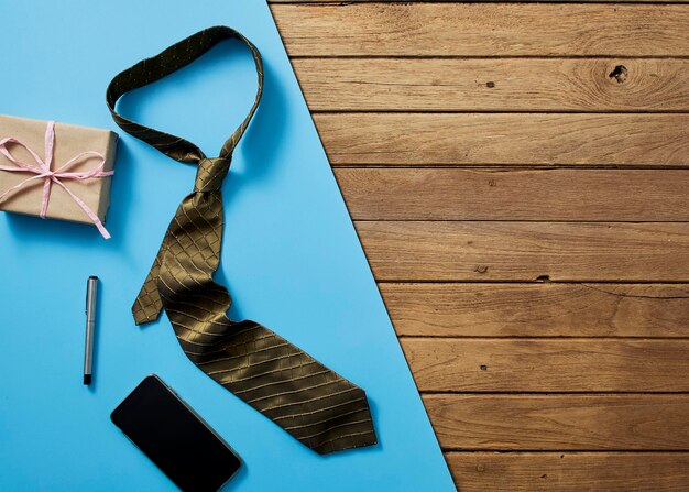 Foto close-up de gravata com telefone celular e presente em uma mesa de madeira