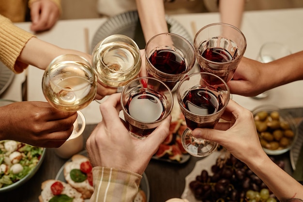 Close-up de grupo de pessoas brindando com taças de vinho na mesa de jantar durante uma festa