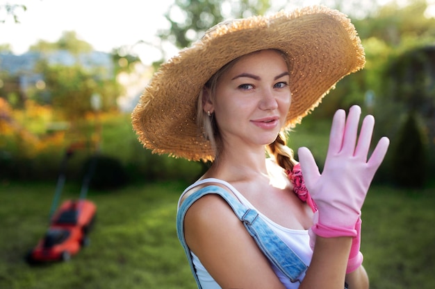 Close-up de jardineiro de mulheres. Uma garota sexy com um chapéu corta a grama perto de casa com um cortador de grama. Projeto paisagístico e cuidado do gramado