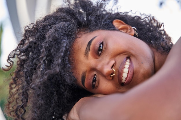 Close-up de jovem latina com cabelo encaracolado e piercing sorrindo olhando para a câmera