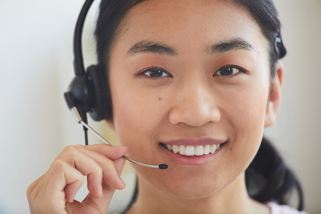 Close-up de jovem operador asiático em fones de ouvido sorrindo