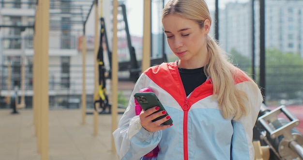 Close-up de jovem usando smartphone verificando aplicativos de fitness em pé no campo de esporte Conceito de estilo de vida saudável
