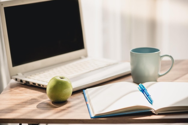 Close-up de laptop com diário por caneca e maçã na mesa