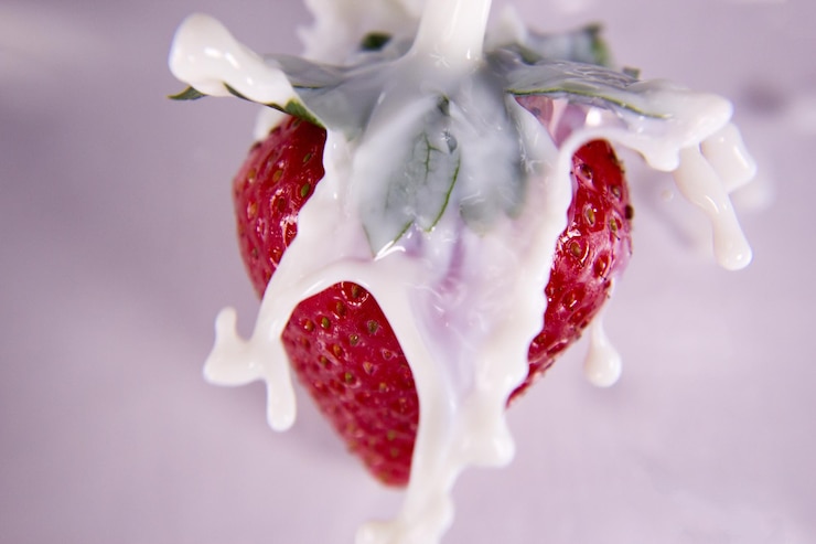 Foto close-up de leite derramando em morango contra fundo branco