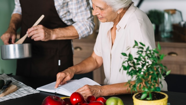 Close-up, de, leitura mulher, livro, sentando, perto, a, homem, preparando alimento, cozinha