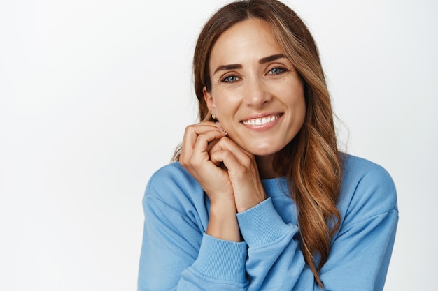 Close-up de linda mulher de meia idade natural, sorrindo dentes brancos, olhando com um olhar adorável, contemplando smth bonito, de pé na blusa contra o fundo branco