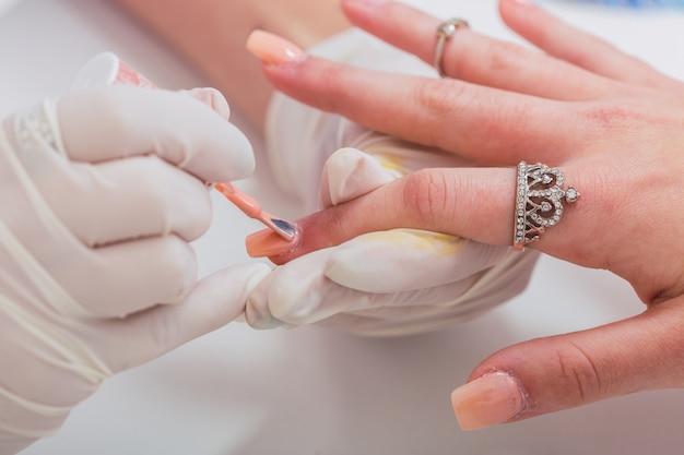 Close-up de manicure profissional embelezando as mãos de uma cliente.