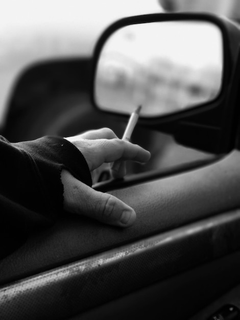 Foto close-up de mão cortada no carro segurando um cigarro