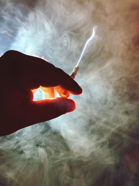 Foto close-up de mão cortada segurando cigarro por fumaça