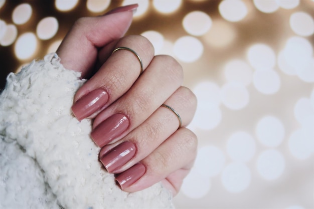 Close-up de mão de mulher com esmalte de unhas contra luz desfocada