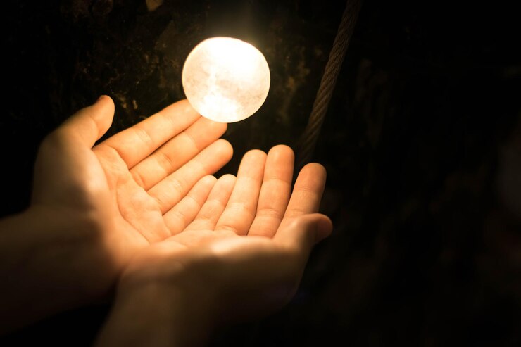 Foto close-up de mão por lâmpada iluminada contra fundo preto