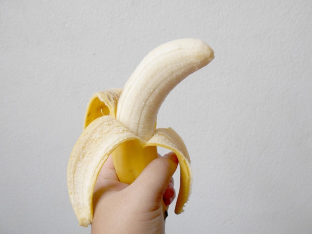 Foto close-up de mão segurando banana contra fundo branco