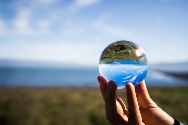 Foto close-up de mão segurando bola de cristal contra o mar e o céu