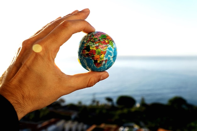 Foto close-up de mão segurando bola de globo contra o mar