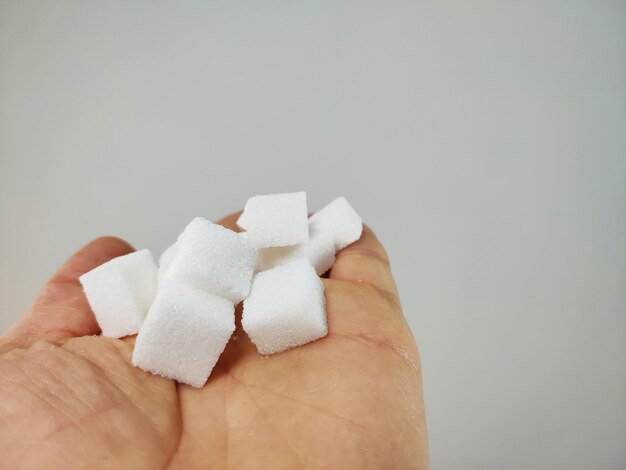 Foto close-up de mão segurando cubos de açúcar contra fundo branco
