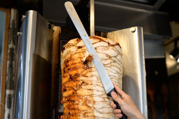 Close-up de mão segurando uma faca cortando o kebab de frango
