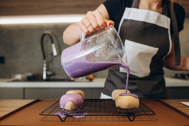 Close-up de mãos de confeiteiro profissional colher o esmalte de chocolate quente de forma desigual sobre os profiteroles para decoração Mulher chef de pastelaria fazendo sobremesas doces e deliciosas