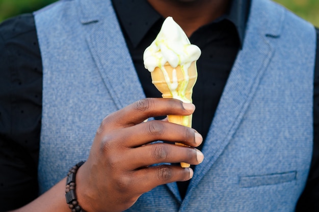 Close-up de mãos de homens negros em trajes elegantes, uma reunião em um parque de verão. empresário hispânico de amigos afro-americanos segurando sorvete doce branco de baunilha em um piquenique de chifre de waffle ao ar livre.