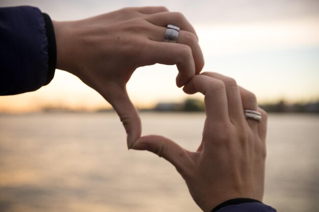 Foto close-up de mãos de mulheres fazendo forma de coração contra o mar durante o pôr do sol