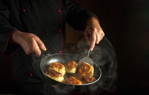 Close-up de mãos de um chef com uma espátula de cozinha e frigideira na cozinha enquanto frita donuts de massa de farinha Espaço preto para publicidade