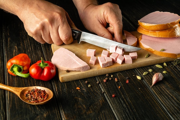 Close-up de mãos de um chef cortando salsicha cozida em pedaços pequenos com uma faca para preparar a carne