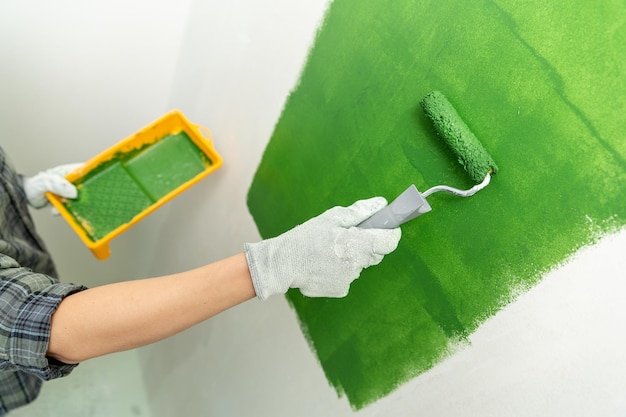 Foto close up de mãos em luvas de trabalho pintando uma parede verde com rolo de tamanho médio