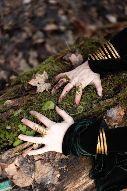 Close-up de mãos femininas com anéis de ouro e pulseira em musgo verde da floresta