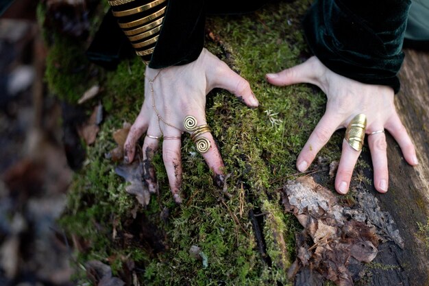 Close-up de mãos femininas com anéis de ouro e pulseira em musgo verde da floresta