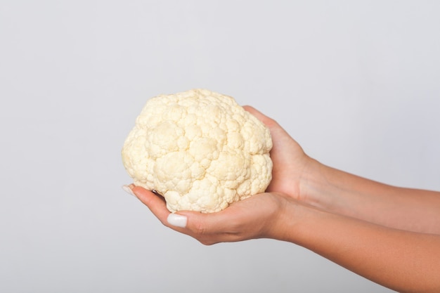 Close-up de mãos femininas segurando couve-flor branca grande, vegetais crus frescos, conceito de alimentação saudável e dieta vegetariana, nutrição alimentar de baixa caloria. estúdio interno tiro isolado em fundo cinza