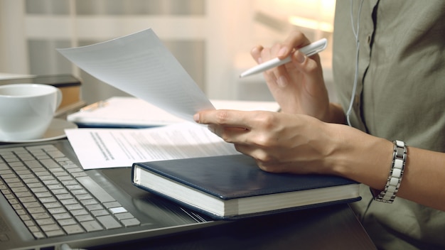 Close-up de mãos femininas segurando um contrato ou relatório financeiro e tomar notas no local de trabalho