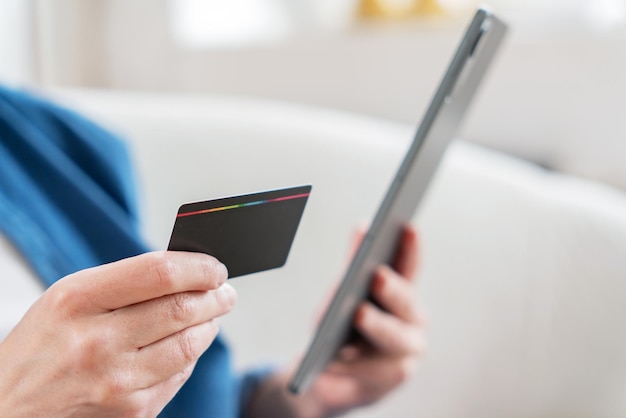Close-up de mãos segurando um cartão de crédito e um tablet sugerindo compras ou serviços bancários on-line