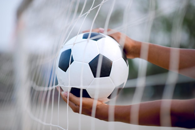 Close-up de mãos segurando uma bola de futebol pela rede no campo de jogo