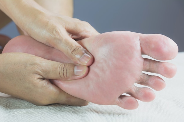 Close-up de massagem nos pés no salão de um fisioterapeuta em uma cama branca.