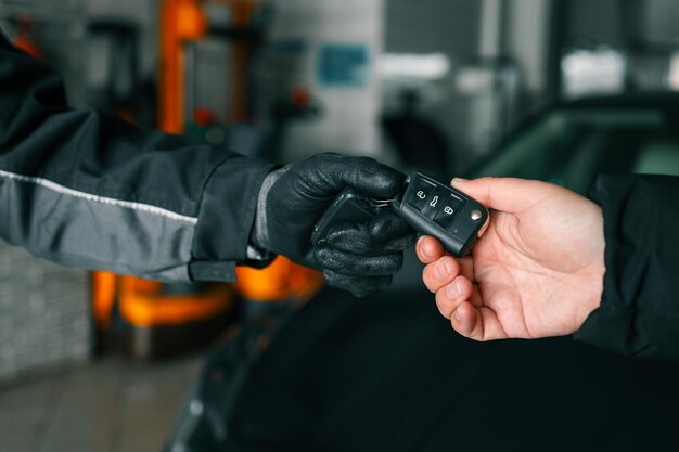 Close-up de mecânico usando luvas entregando chaves de carro a um cliente em uma oficina de reparação simbolizando serviço e manutenção de veículos
