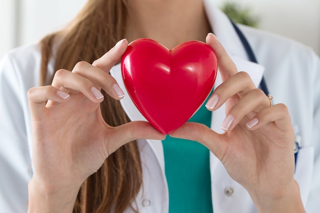 Close-up de médico feminino mãos segurando ler coração. Cuidados de saúde, cardiologia e conceito médico