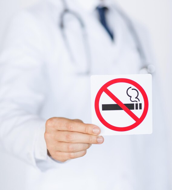 Close-up de médico segurando placa de proibido fumar nas mãos