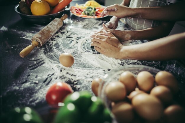 Close-up de menina e suas mãos de mãe achatando a massa usando um rolo na cozinha