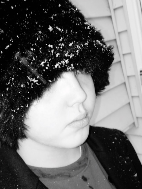 Close-up de menino vestindo chapéu de pele de urso com flocos de neve