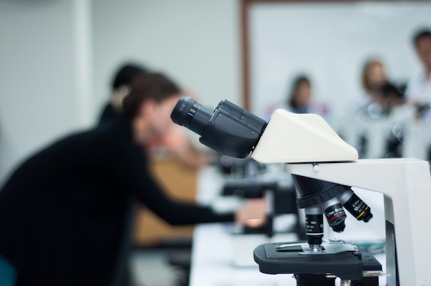 Close-up de microscópio com cientistas em segundo plano no laboratório