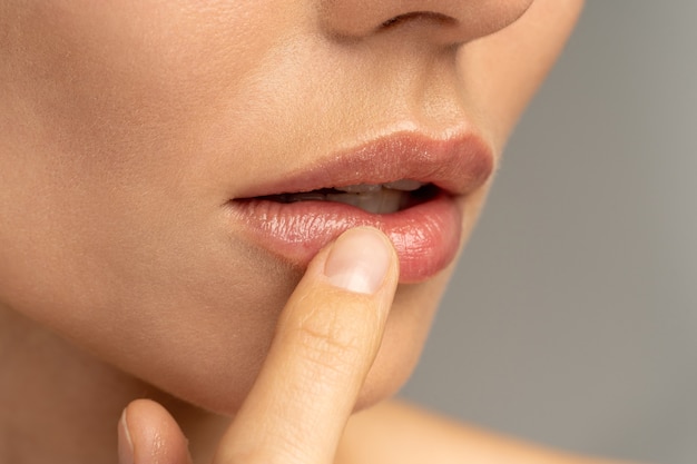 Close-up de mulher aplicando bálsamo hidratante e nutritivo aos lábios com o dedo