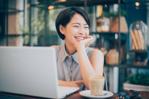 Close-up de mulher bonita sorridente com laptop e xícara de café na mesa