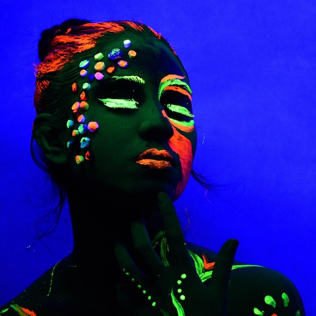 Close-up de mulher com pintura facial vibrante contra fundo azul