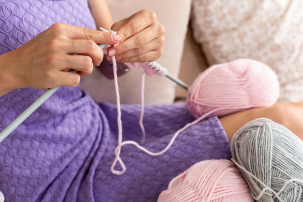 Close-up de mulher com um vestido lilás para casa tricota um lenço rosa claro ou xadrez de fios naturais na cama.