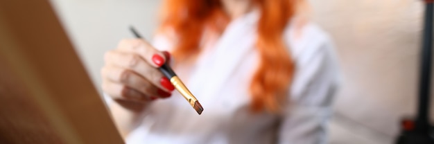 Close-up de mulher de cabelo vermelho segurando o pincel com tinta a óleo.