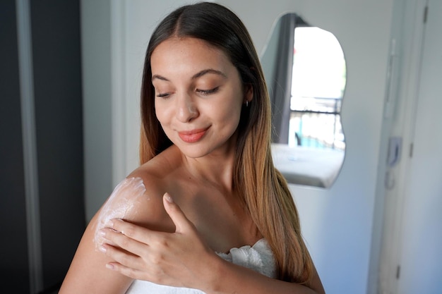 Close-up de mulher hispânica aplicando loção hidratante no ombro em casa