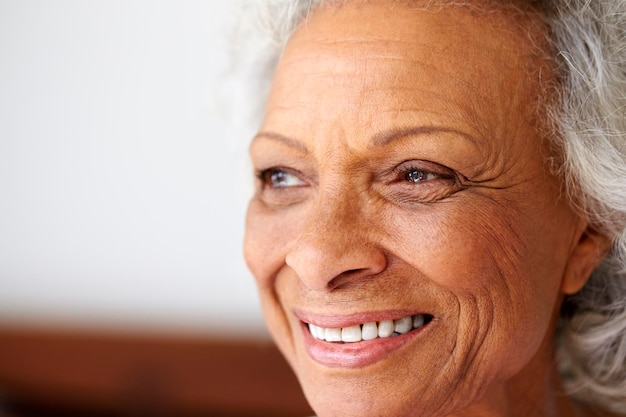 Close-up de mulher idosa sorridente, sentada na cama em casa, olhando positivo