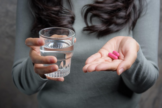 Close-up de mulher segurando pílula e copo de água